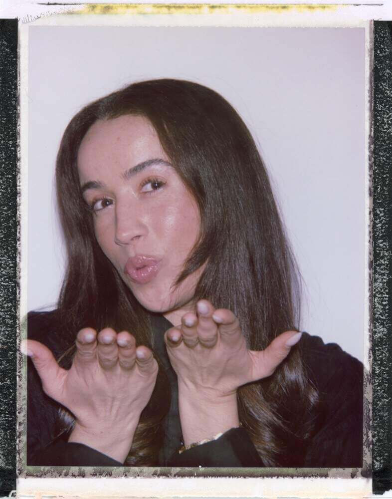 That Good Co A person with long hair, embodying the spirit of That Good Co, blows a kiss with both hands toward the camera against a plain background.