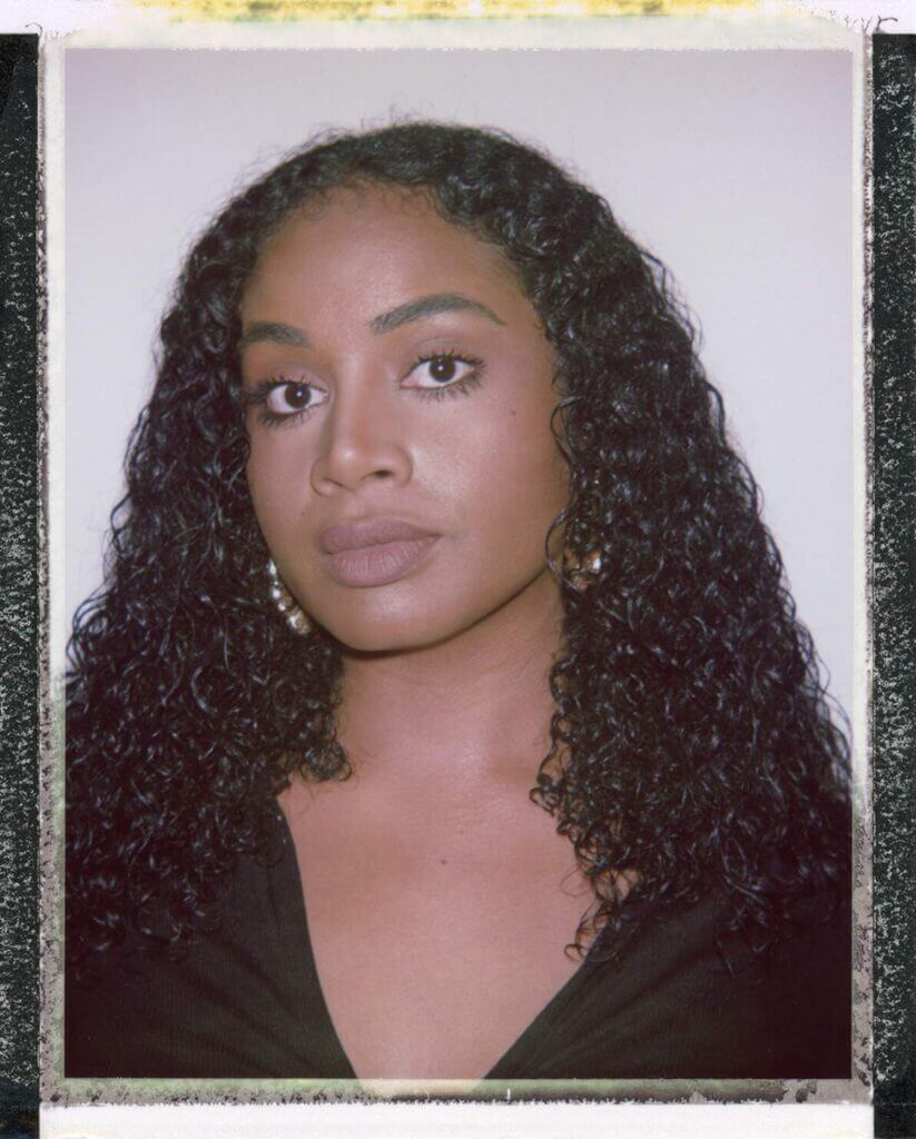 That Good Co A person with long curly hair, wearing a black top from That Good Co, looks directly at the camera against a plain background.