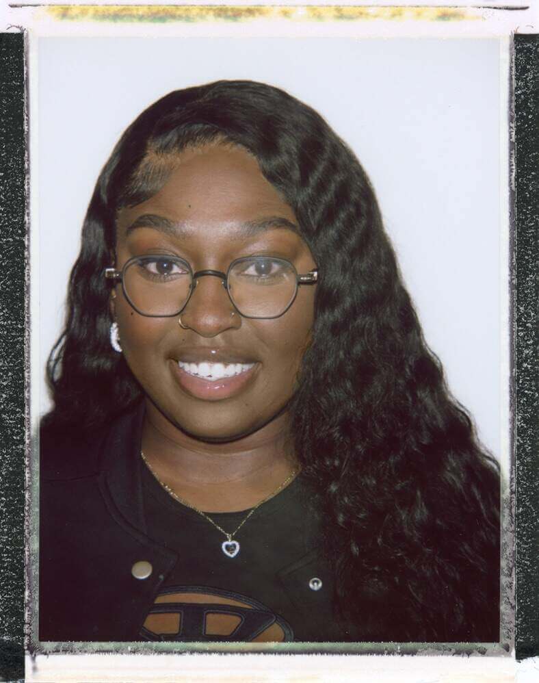 That Good Co A person with long curly hair, wearing glasses and a nose ring, smiles at the camera, embodying the confident spirit of That Good Co.