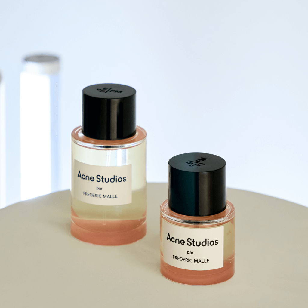 That Good Co Two Acne Studios par Frederic Malle perfume bottles rest elegantly on a beige surface, with a soft background light, perfectly capturing the essence of That Good Co's refined aesthetic.