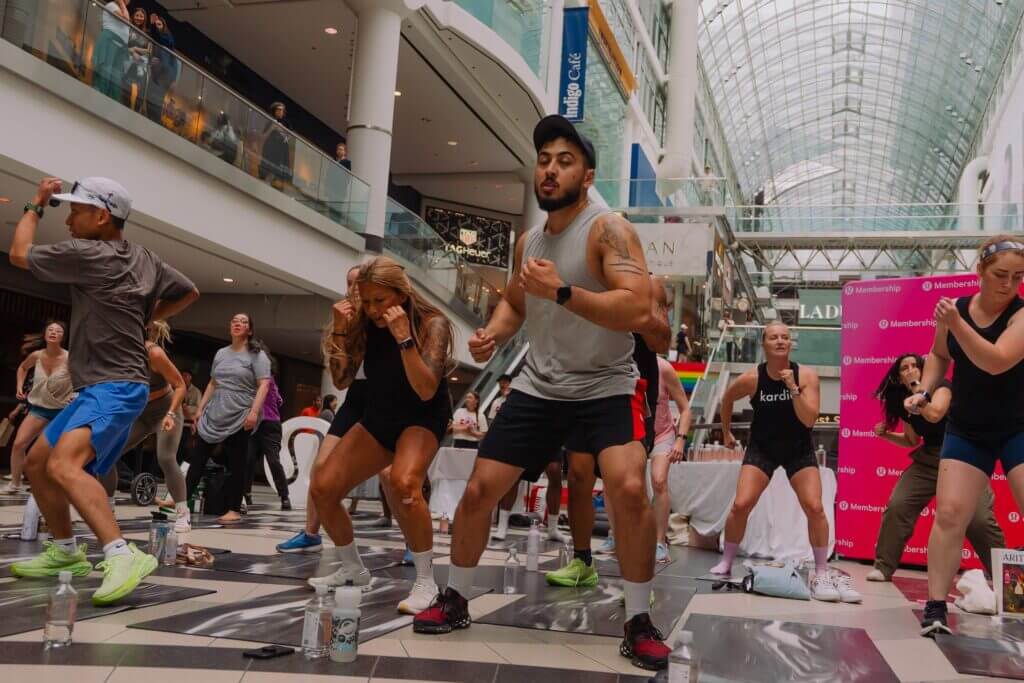 That Good Co People participating in a That Good Co group fitness class inside a shopping mall. Participants are wearing athletic clothing and exercising energetically.