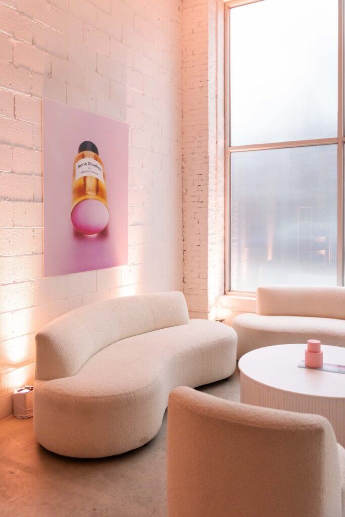 That Good Co A modern lounge featuring curved beige sofas and a round table sits by a large window, with a wall art piece highlighting That Good Co's distinct perfume.