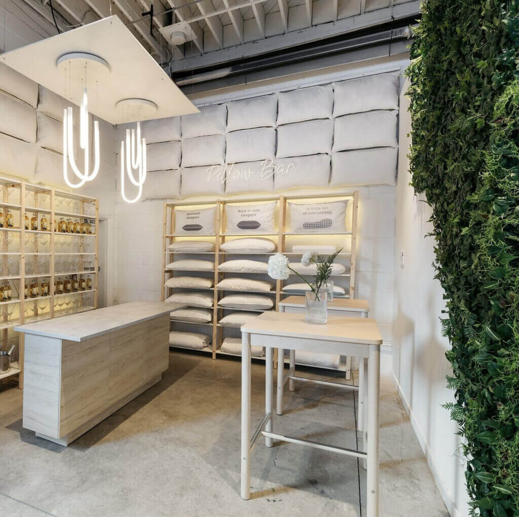 That Good Co The modern That Good Co store interior features a stylish pillow display, wooden tables, sleek pendant lights, and a lush wall covered in greenery.