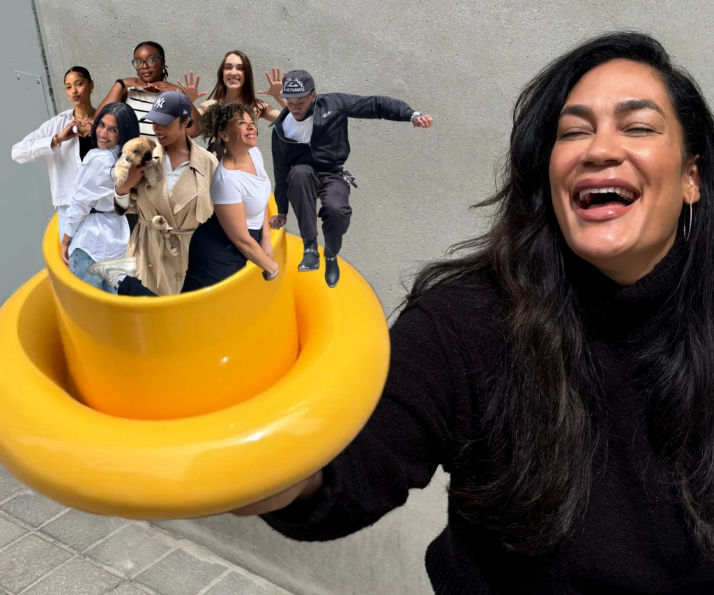 That Good Co A woman smiles and holds a large yellow hat; inside the hat are several people posing in various stances, digitally edited to appear miniature.
