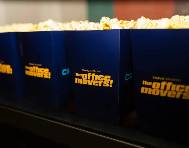 That Good Co Blue popcorn containers labeled "The Office Movers! Crave Original" are lined up, filled with popcorn.