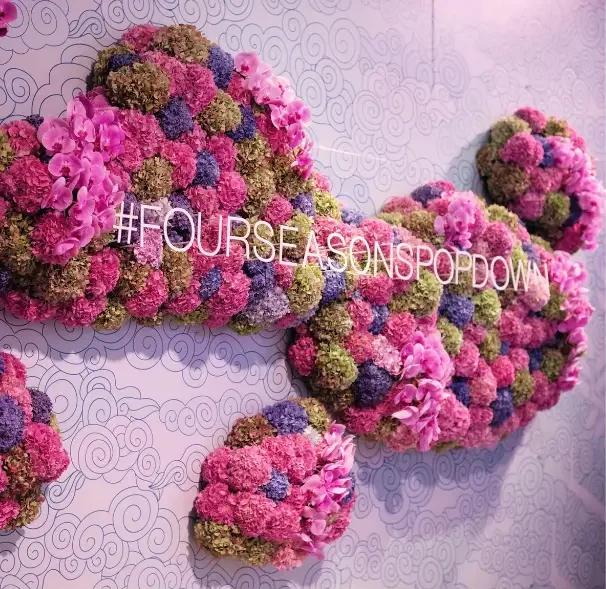 That Good Co A wall display of colorful flower clusters forms a bone shape with the text “#FOURSEASONSPOPDOWN” in white letters across it, set against a patterned background.