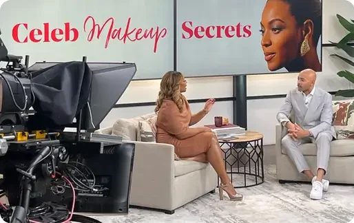 That Good Co Two people sit on a studio set having a conversation. Behind them, a screen displays the text "Celeb Makeup Secrets" and a woman's face. A camera is visible in the foreground.
